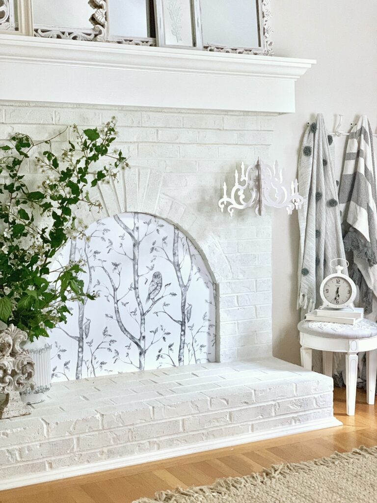 A white brick fireplace with a fireplace cover that has a woodland black and white print on it. 