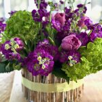 A purple and green centerpiece in a twig covered container.