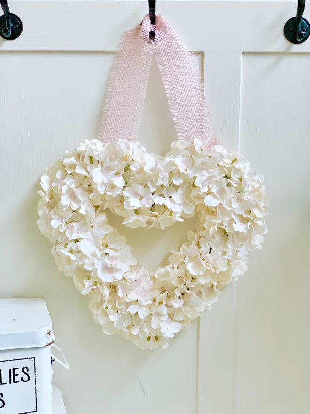 Soft cream hydrangea with hints of pink on a heart shaped wreath with a pink ribbon for hanging.