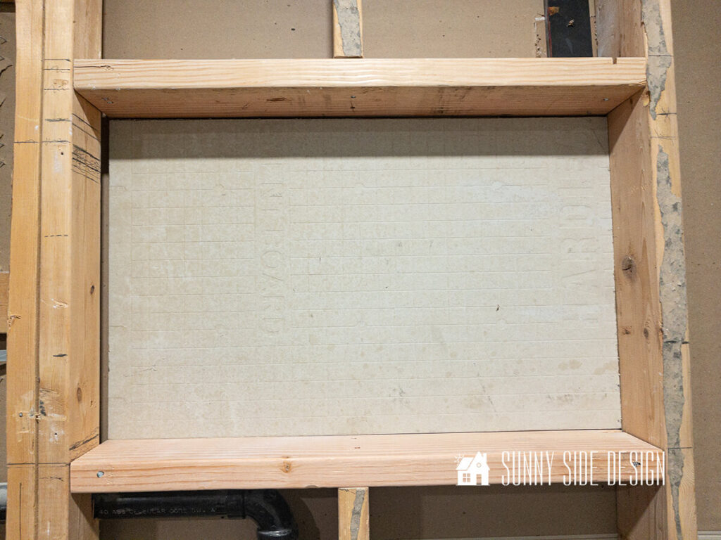 Cement backer board is secured to the back of the shower niche with construction adhesive.