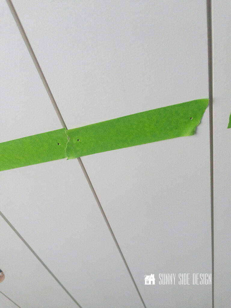 Green painters tape applied to shiplap with brad nails installed through the tape.